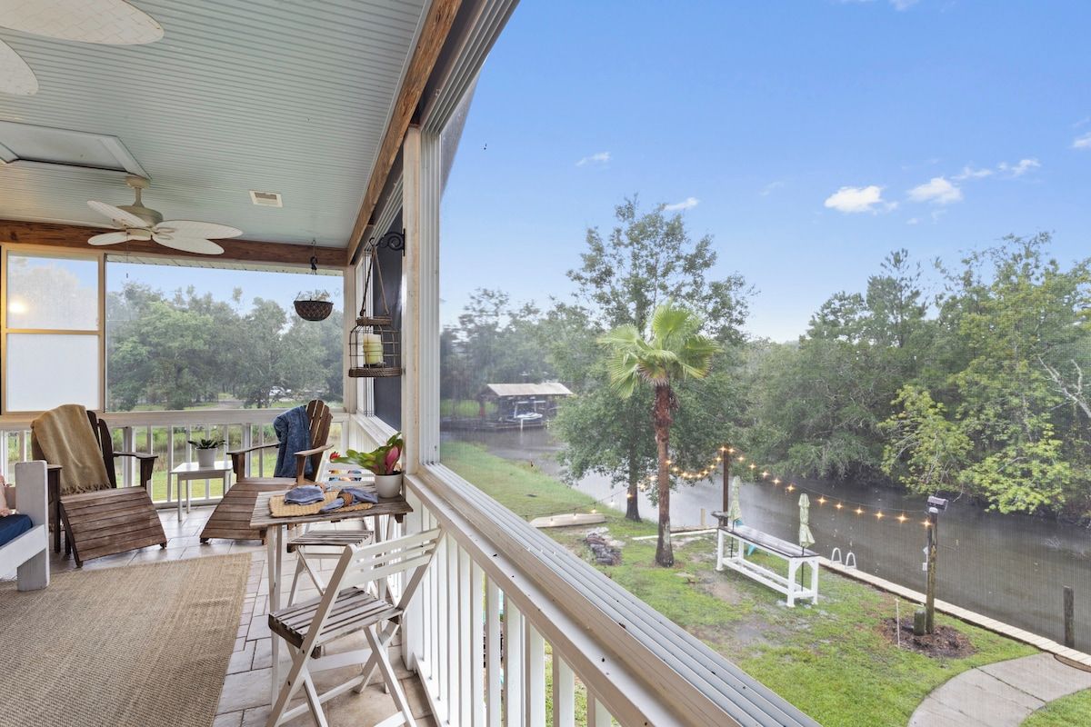 A balcony with a view of a river, outdoor furniture, and a ceiling fan.
