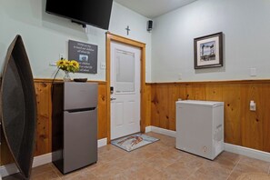 Une cuisine équipée d’un réfrigérateur, d’un petit appareil électroménager, de lambris en bois, d’une porte, d’un tableau encadré et d’un téléviseur fixé au mur.