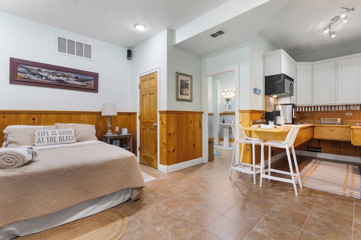 A bedroom with a bed, a desk, and a kitchenette.