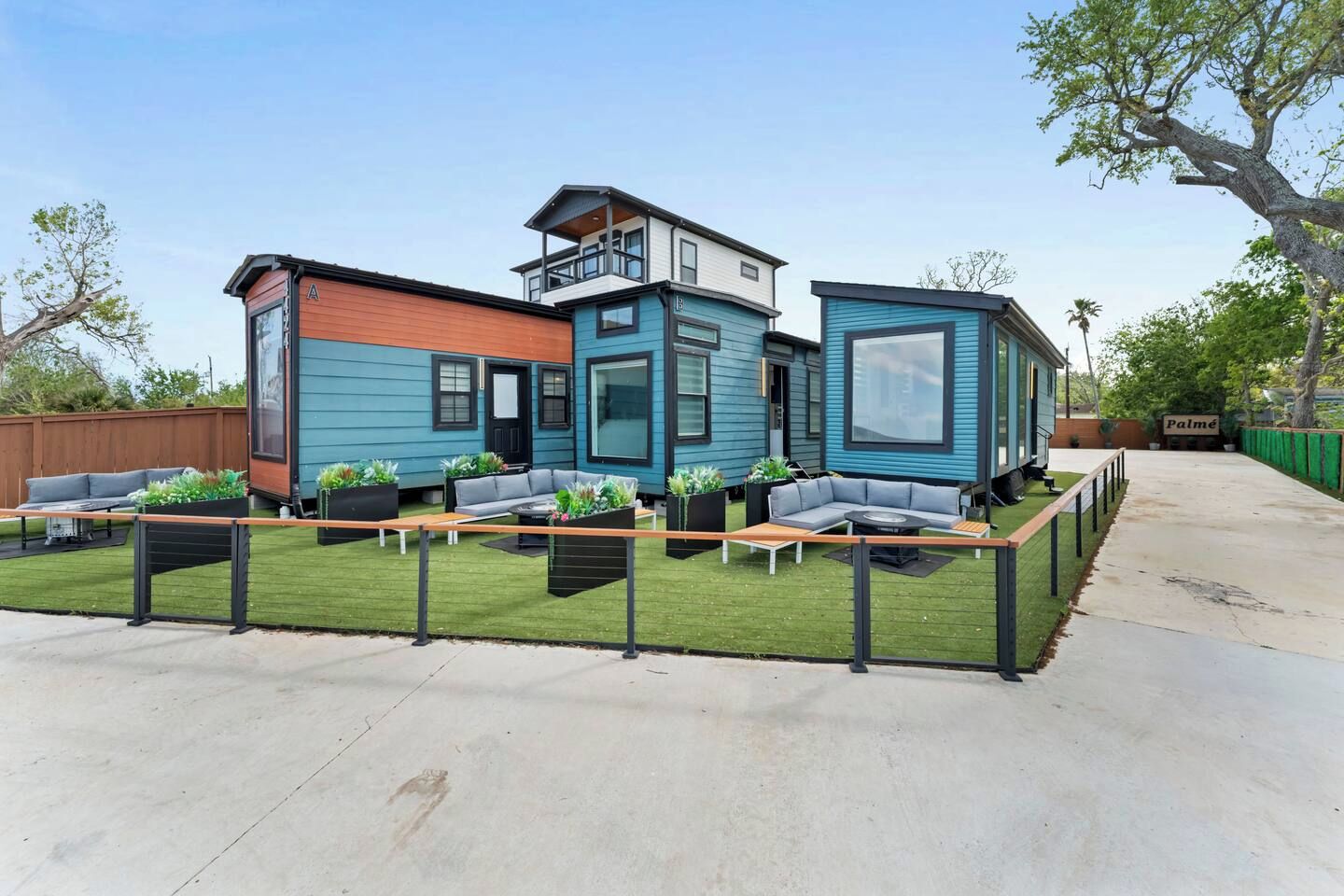 A modern house with a flat roof, a balcony, and a fenced backyard with outdoor seating.