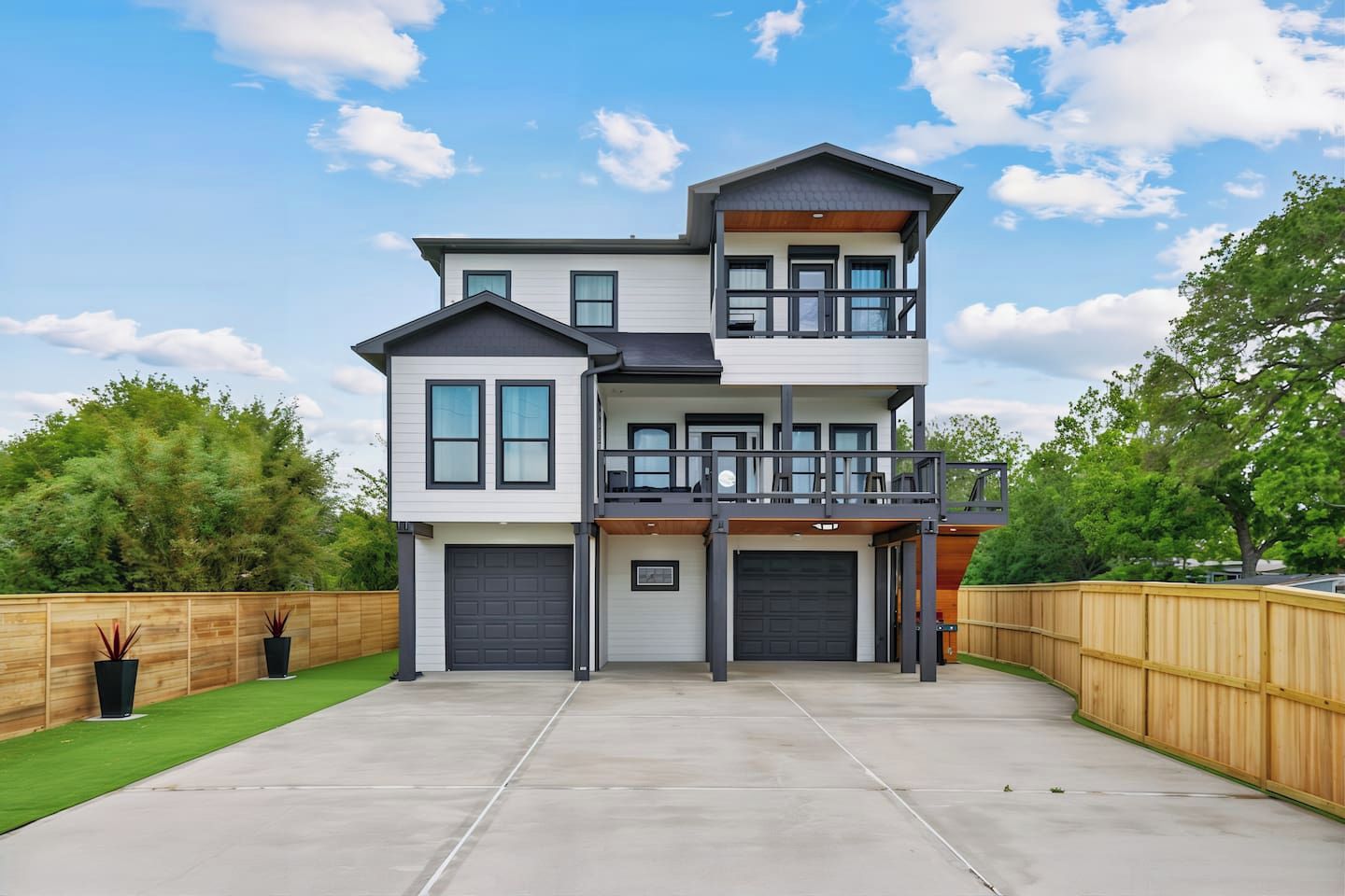 A two-story house with a front garage, a balcony on the upper level, and a wooden fence surrounding the property.