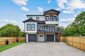 A two-story house with a front garage, a balcony on the upper level, and a wooden fence surrounding the property. - Palmé Bay | 3 Entire Waterfront Tiny Homes + Pool (Bacliff)