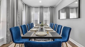 A dining room with a long table set for six, blue chairs, and a modern chandelier. - Palme Bayfront Estate | 4 Homes, Pool + Hot Tub (Bacliff)