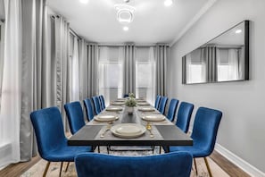 Comedor con una larga mesa dispuesta para seis comensales, sillas azules y una lámpara de araña moderna.
