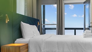 A modern hotel room with a large bed, a wooden nightstand, and a view of the sea through large windows. - Palme Bayfront Estate | 4 Homes, Pool + Hot Tub (Bacliff)