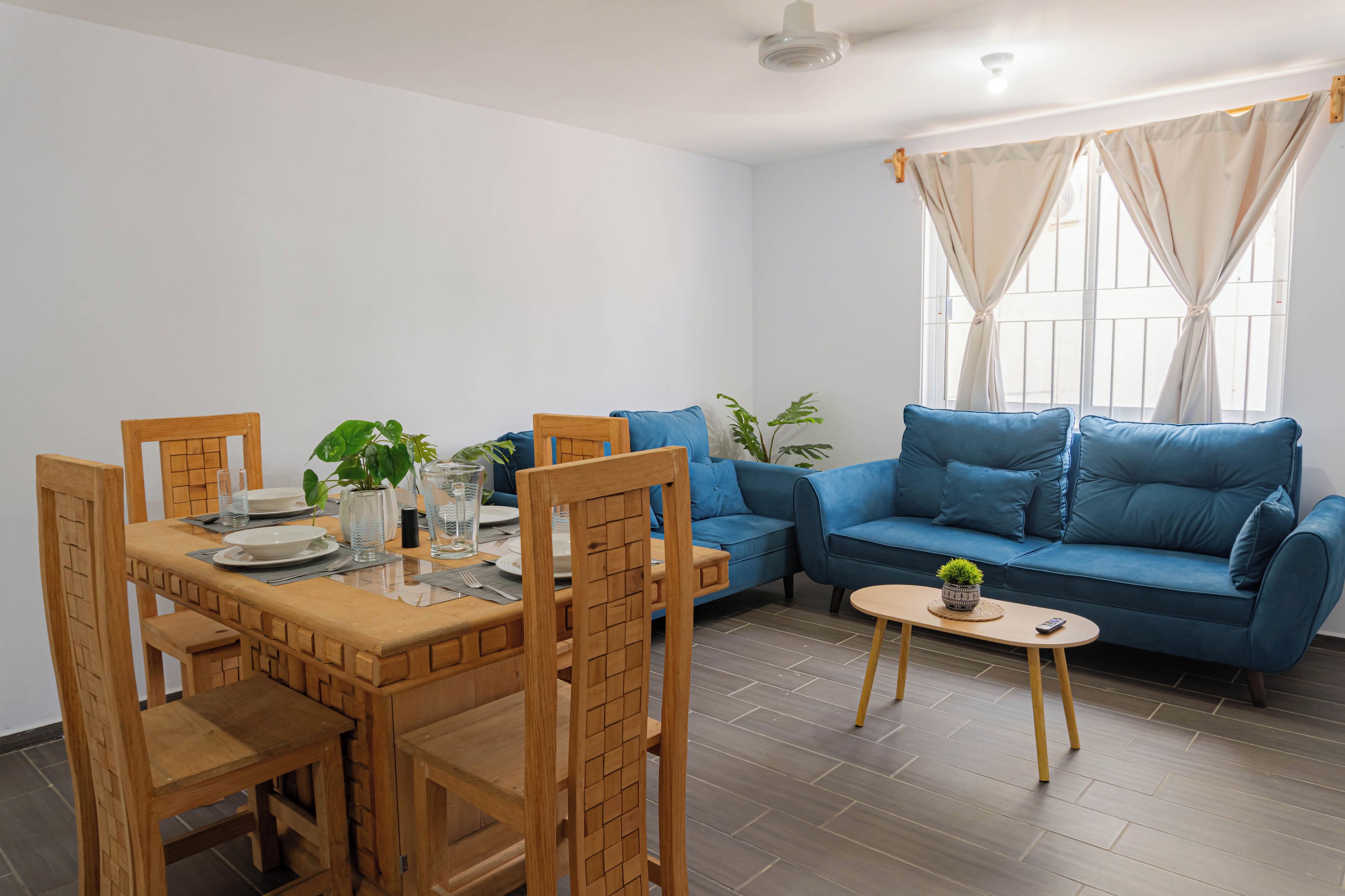 Ein modernes Wohnzimmer mit Essbereich, ausgestattet mit einem blauen Sofa, einem Holzesstisch und Stühlen.