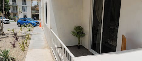 A residential building with a balcony, a parked blue car, and a potted plant.