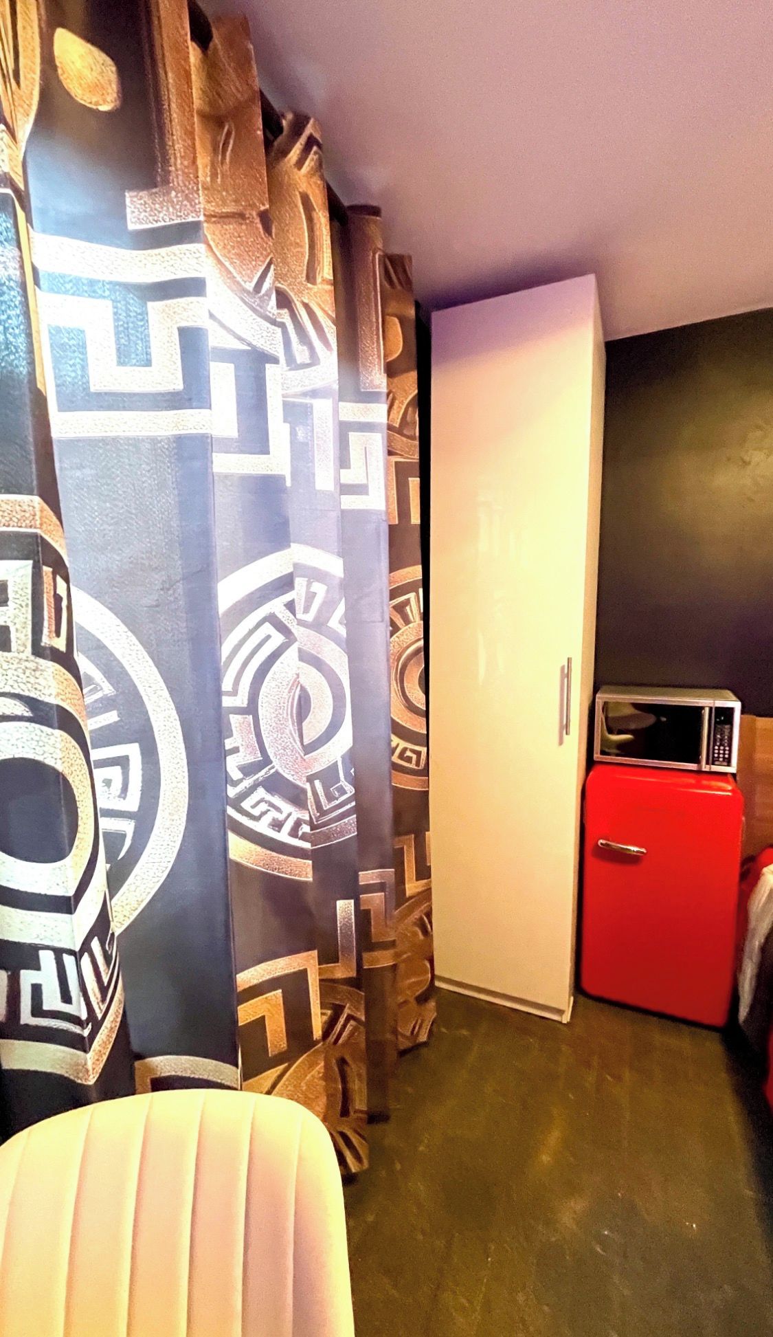 Une pièce avec un rideau à motifs, une porte blanche et un appareil électroménager rouge.