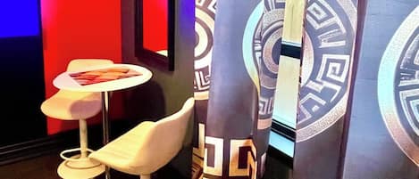 Une pièce avec un mur rouge, une petite table blanche avec une chaise, et des rideaux à motifs.