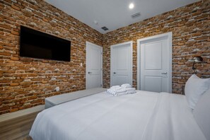 Ein Hotelzimmer mit einer Ziegelwand, einem Bett mit weißen Leinen und einem an der Wand befestigten Flachbildfernseher.