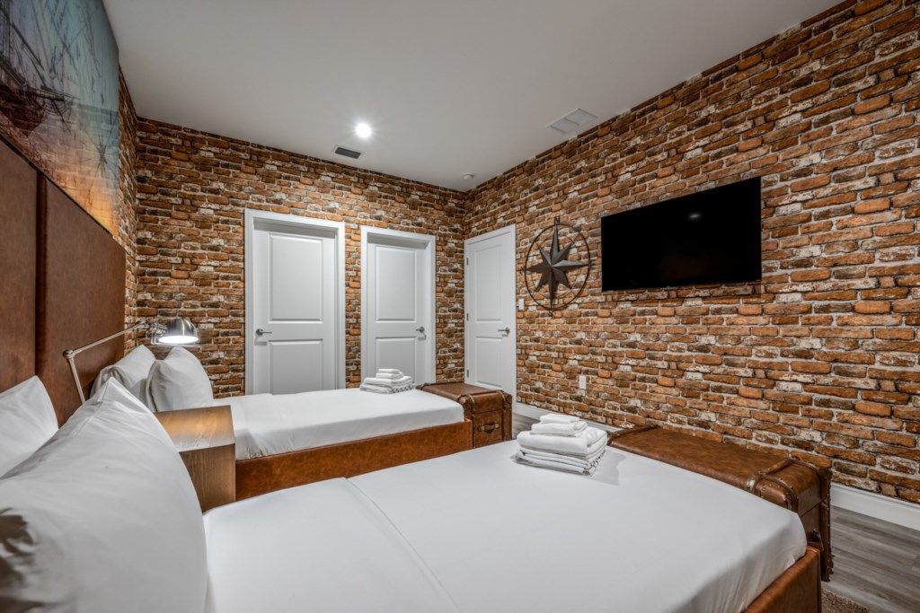 A hotel room with a brick wall, two beds, a TV, and a coat rack.