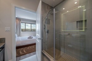 Une chambre d’hôtel moderne dotée d’une douche en verre, d’un lit avec vue et d’une petite fenêtre.