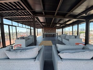 Amplia sala de estar con sofás grises y una barra, ventanas grandes con vistas a la ciudad.