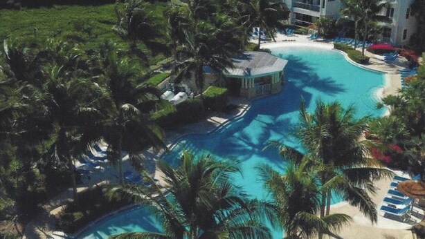 Ein Resort mit einem großen Schwimmbad, umgeben von Palmen und Liegestühlen.