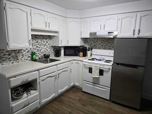 A kitchen with white cabinets, a microwave, a stove, and a refrigerator.
