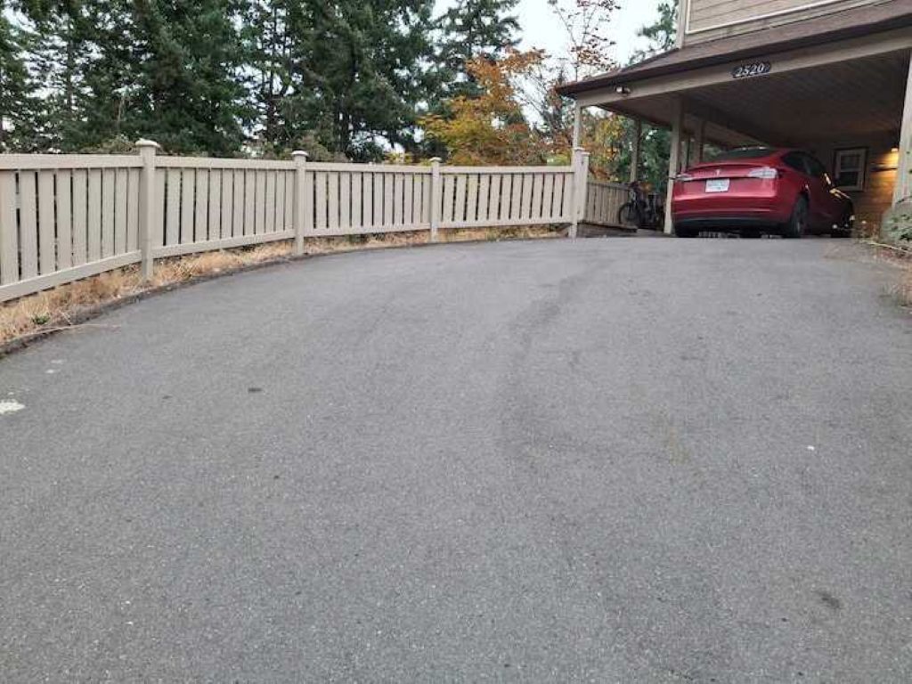 Uma entrada pavimentada leva a uma garagem onde um carro vermelho está estacionado.
