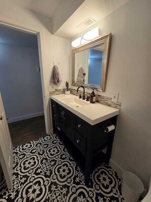 Un bagno con un lavandino bianco, mobili scuri, uno specchio illuminato e piastrelle a motivi decorativi.