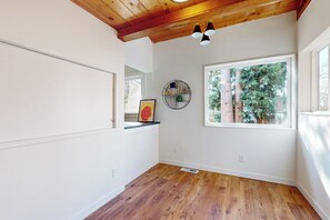 Ein Zimmer mit Holzboden, einem großen Fenster mit Blick auf Bäume, einer Decke mit freiliegenden Balken und einer wandmontierten Leuchte.