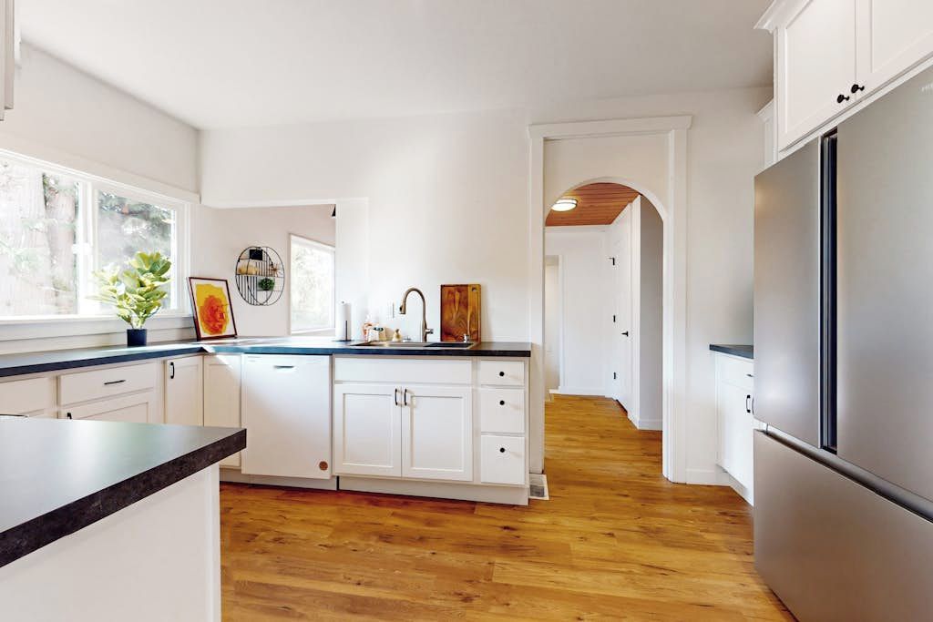 A modern kitchen with white cabinetry, a stainless steel refrigerator, and a wooden floor.