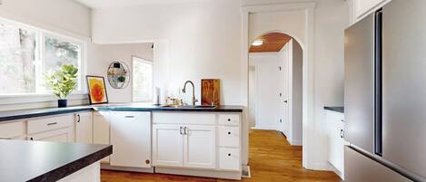 A modern kitchen with white cabinetry, a stainless steel refrigerator, and a wooden floor.