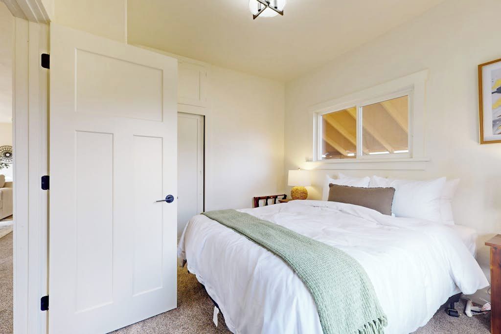 Een slaapkamer met een bed, een raam, een deur en een nachtkastje.