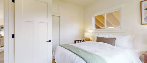 Un dormitorio con cama, ventana, puerta y mesita de noche.