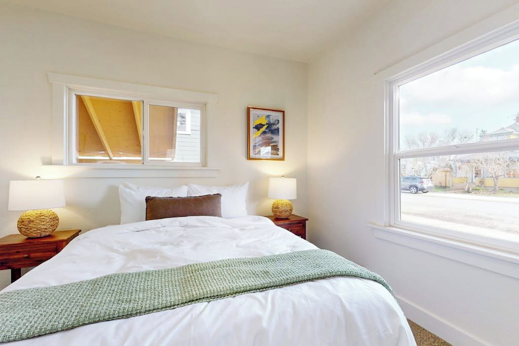 A hotel room with a large bed, two bedside lamps, a window with a view, and a framed picture on the wall.