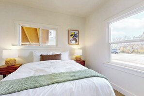 Ett hotellrum med en stor säng, två sänglampor, ett fönster med utsikt och en inramad tavla på väggen.