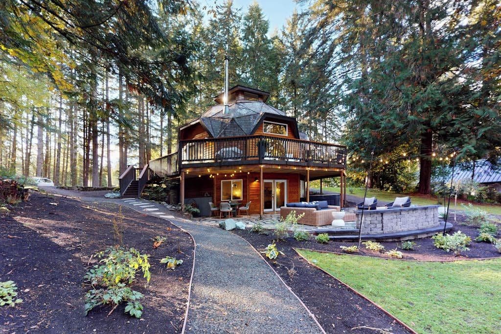 Une cabane à deux étages avec une terrasse, entourée d’une forêt.