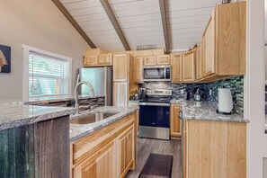 A kitchen with wooden cabinets, granite countertops, stainless steel appliances, and a window with blinds. - 2BR riverfront gem with kayaks & hot tub - dogs ok (Tahuya)