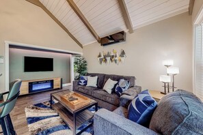 A modern living room with a flat-screen TV, a sofa, a coffee table, and a lamp. - 2BR riverfront gem with kayaks & hot tub - dogs ok (Tahuya)