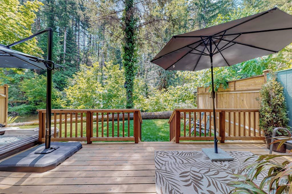 A wooden deck with a patio umbrella, a seating area, and a view of a forested area.