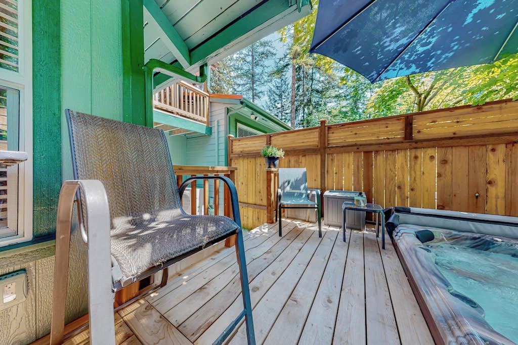 A wooden deck with a hot tub, outdoor seating, and a covered area with a table and chairs.