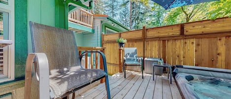 Eine Holzterrasse mit Whirlpool, Sitzgelegenheiten im Freien und einem überdachten Bereich mit Tisch und Stühlen.