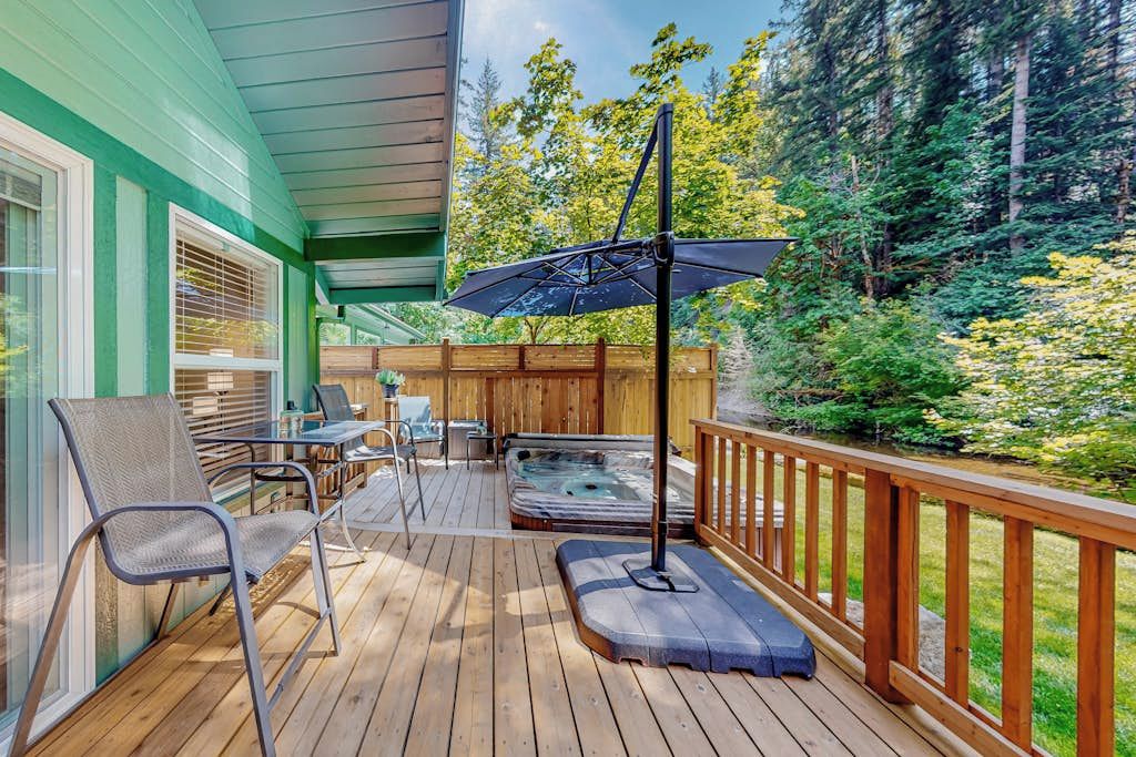 Eine Holzterrasse mit Gartenmöbeln, einem Whirlpool und einer Pergola mit Sonnenschirm.