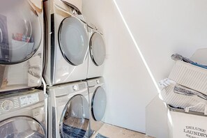 A laundry area with stacked washing machines and a basket of folded clothes. - 2BR riverfront gem with kayaks & hot tub - dogs ok (Tahuya)