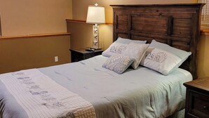 A neatly made bed with a patterned bedspread and pillows, a bedside lamp, and a wooden headboard. - 1BR with fireplace and Puget Sound and Mt. Baker views (Port Ludlow)