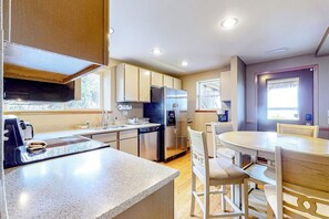 A modern kitchen with a central island, built-in appliances, and a dining area with a round table and chairs. - 1BR with fireplace and Puget Sound and Mt. Baker views (Port Ludlow)