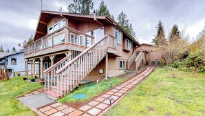 A two-story wooden house with a balcony and a staircase leading to the upper floor. - 1BR with fireplace and Puget Sound and Mt. Baker views (Port Ludlow)