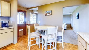 A compact kitchen with a round dining table and white chairs, a coffee machine, and a view through an open door. - 1BR with fireplace and Puget Sound and Mt. Baker views (Port Ludlow)
