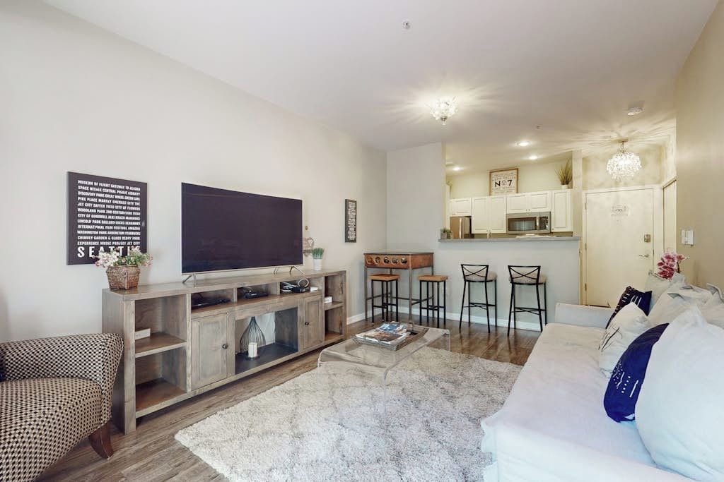 Ein Wohnzimmer mit Flachbildfernseher, Sofa, Couchtisch und einer Küche im Hintergrund.