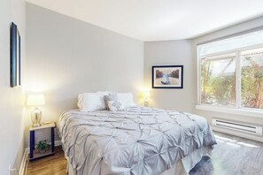 A bedroom with a bed, bedside lamps, a framed picture on the wall, and a window. - Walkable 1BR Soundview Washington State Conv.Cente (Seattle)