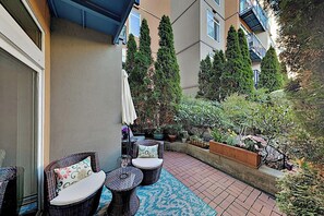 A patio with wicker furniture, potted plants, and a view of neighboring buildings. - Walkable 1BR Soundview Washington State Conv.Cente (Seattle)