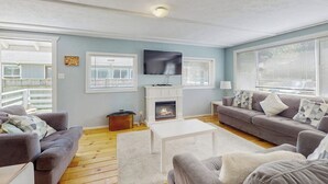 Ein Wohnzimmer mit Kamin, zwei Sofas, einem Fernseher und großen Fenstern.