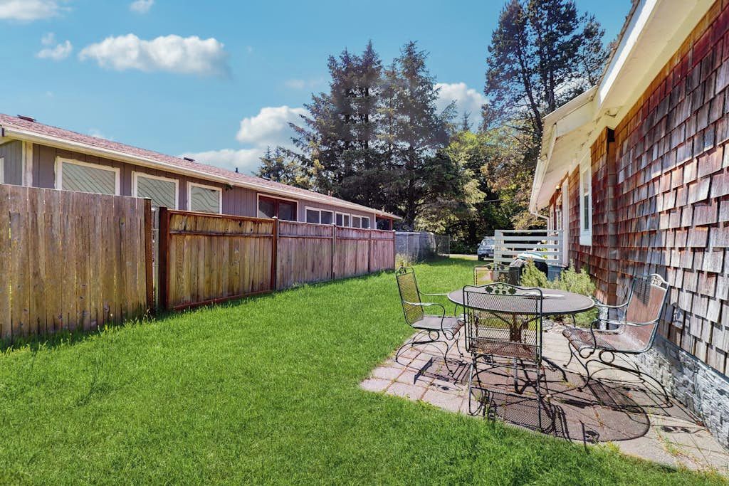 Un jardin avec une table et des chaises de patio, une clôture en bois et un bâtiment dont l’extérieur est recouvert de bardeaux.