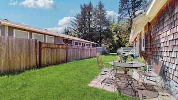 Un jardin avec une table et des chaises de patio, une clôture en bois et un bâtiment dont l’extérieur est recouvert de bardeaux.