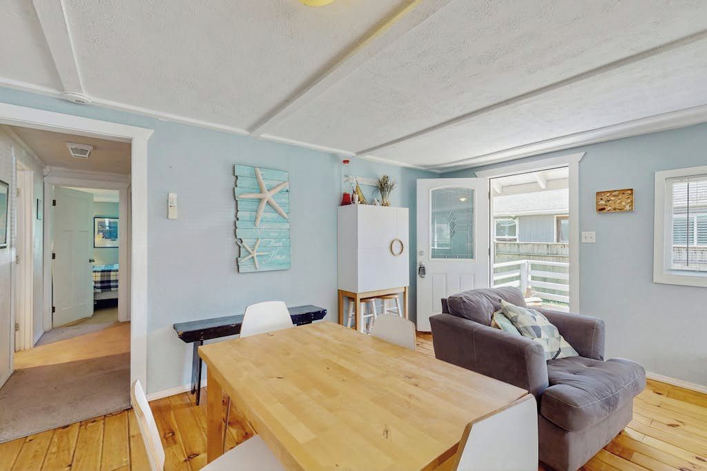 Una habitación con una mesa de comedor de madera, un sofá gris, un armario blanco y una decoración de estrella de mar en la pared.