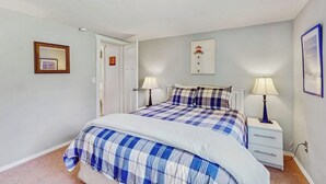 Ein Schlafzimmer mit einem Bett, zwei Nachttischen, einer Tür und einem an der Wand hängenden Bild.