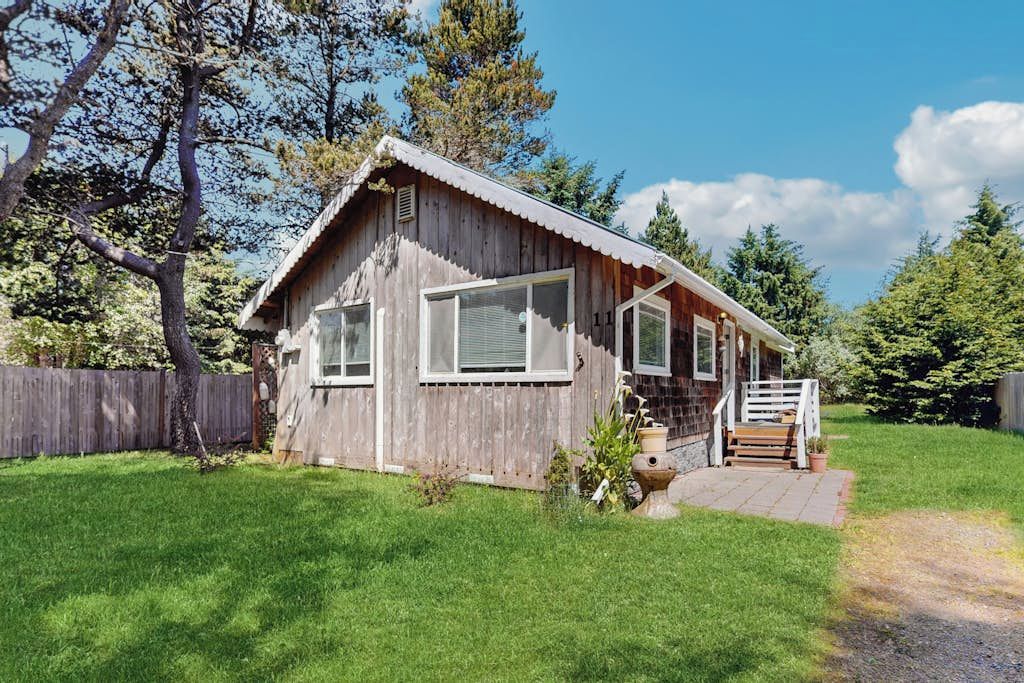 Une cabane en bois dotée d’un porche, de grandes fenêtres et d’une cour clôturée.