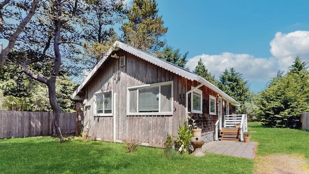 Eine Holzhütte mit Veranda, großen Fenstern und einem eingezäunten Garten.